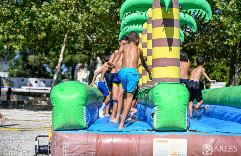 Image d'enfants jouant sur des structures gonflables permettant des jeux de glisse aquatiques le 29 juillet 2026 dans le quartier de Barriol. Photo : Jan Dyver / Ville d'Arles.