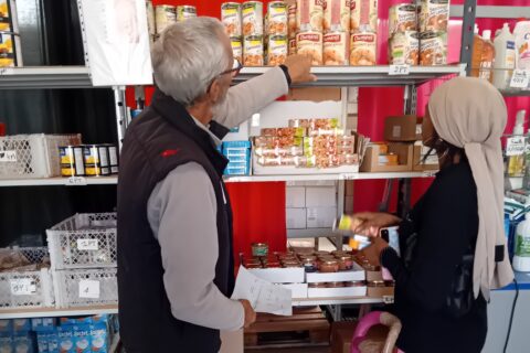Photo prise dans les locaux des Restos du Cœur à Arles sur le parcours de distribution où l'on voit une bénéficiaire accompagnée d'un bénévole. Photo : Ville d'Arles.